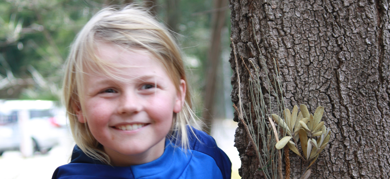 young person smiling standing next to a tree