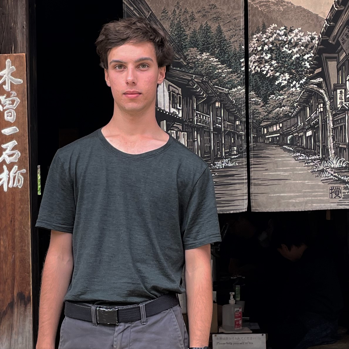 Photo of Enzo Munro, standing in front of a painted streetscape. 