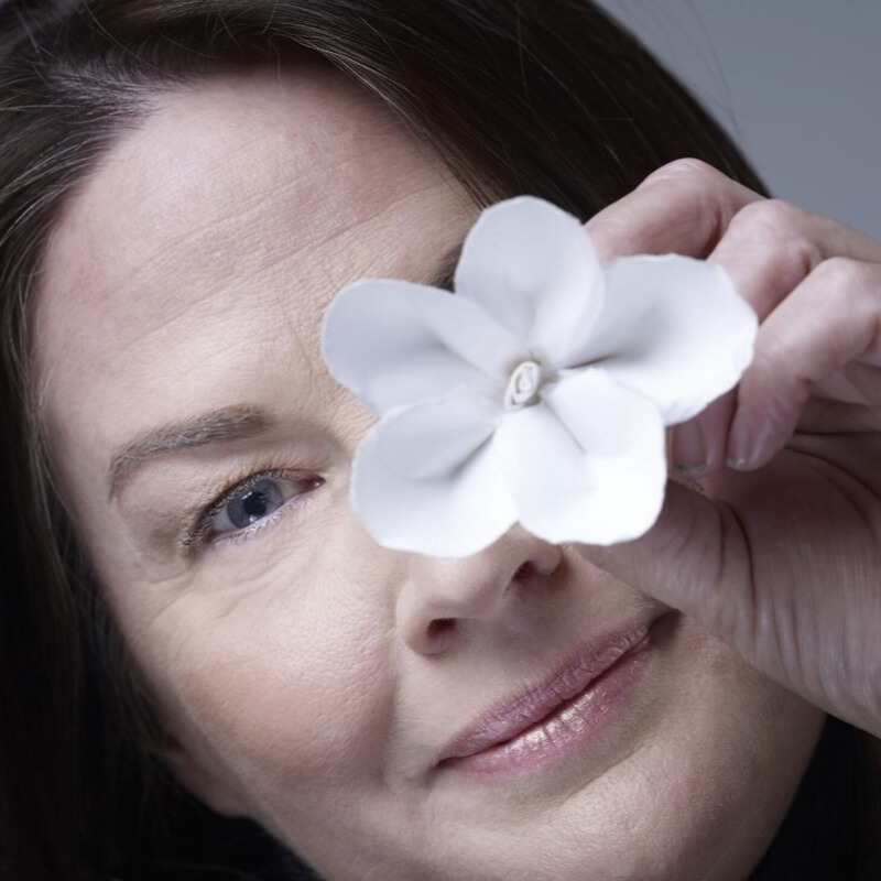 Photo portrait of Jo Neville holding a paper flower in front of her eye