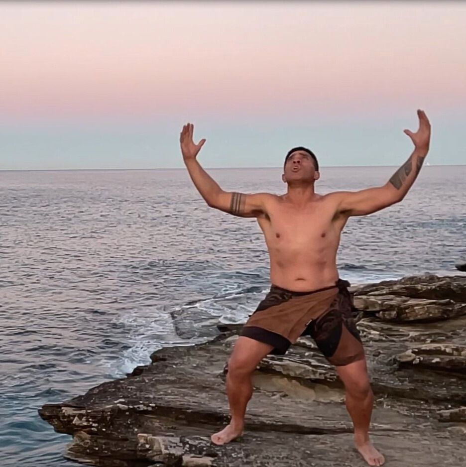 Male Polynesian dancer performs on a cliff overlooking the ocean at sunrise.