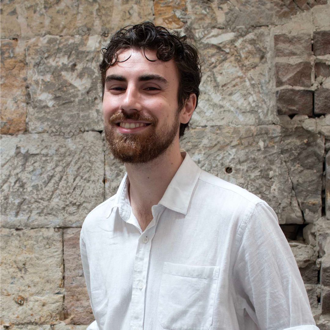Photo of Daniel Press, smiling, with a beard and brown curly hair, wearing a white button up shirt.