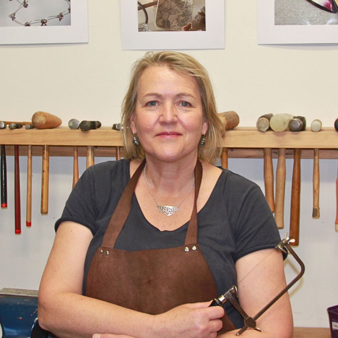 Photo of Susan Peacock, with silversmith hammers behind her on a wall rack