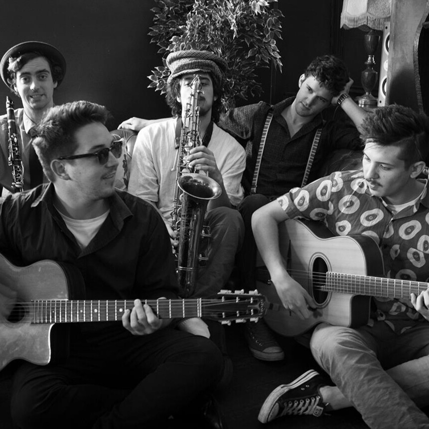 Photo of the band sitting on a couch, playing or holding their instruments.