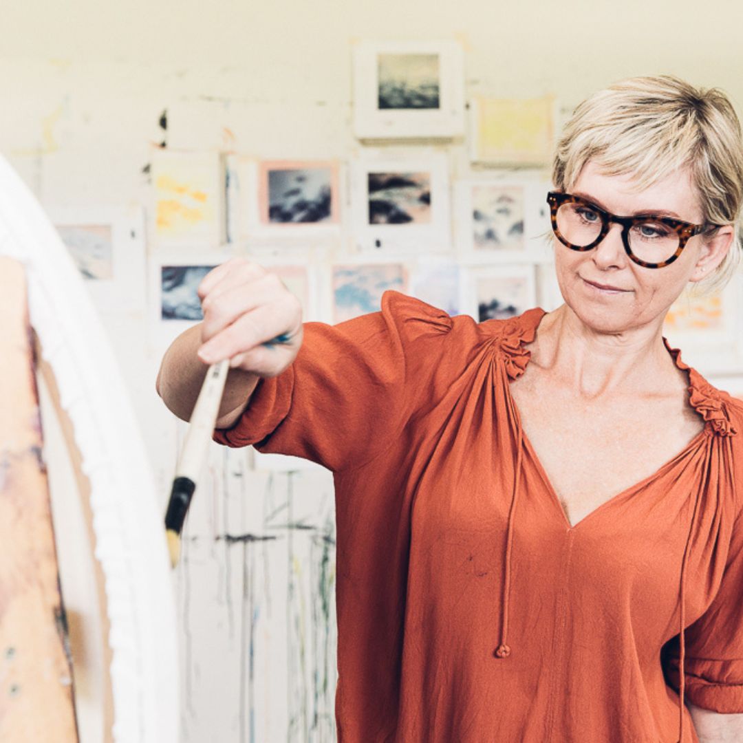 Susie stands at an easel, focused on painting the canvas in front of her. 