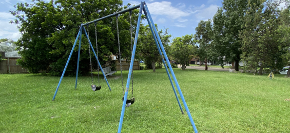 swing set on grass reserve, trees and bench seat