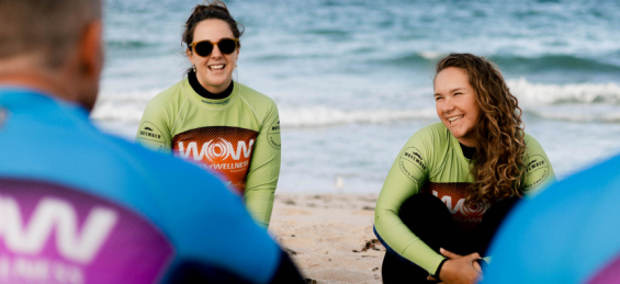 Two people sitting on the beach with a surfing instructor