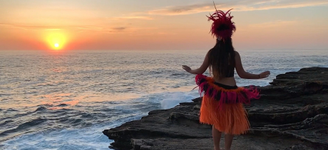 Screenshot from the video artwork Pakoko, showing a female Polynesian dancer performing on the cliffs next to the ocean at sunrise.