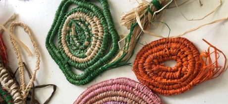 Photo of three hand-woven shapes using rafia. A large pink oval at the bottom, a smaller red oval on the right, and a small green star on the top left. 