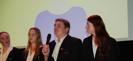 Young people speaking on stage with a mic