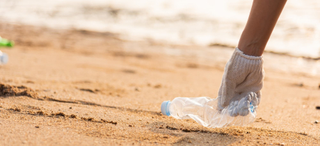 Someone picking up a plastic bottle from the beach