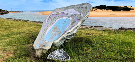 Metal shell artwork on grass next to beach