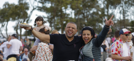 A couple  with a plate of food and smiling amongst a crowd of people