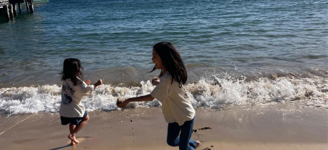 Two people handing hands jumping by the ocean
