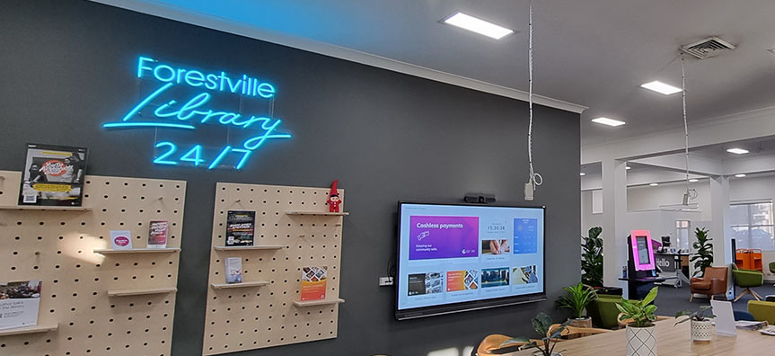 A blue neon sign says Forestville Library 24/7 above a space in the library