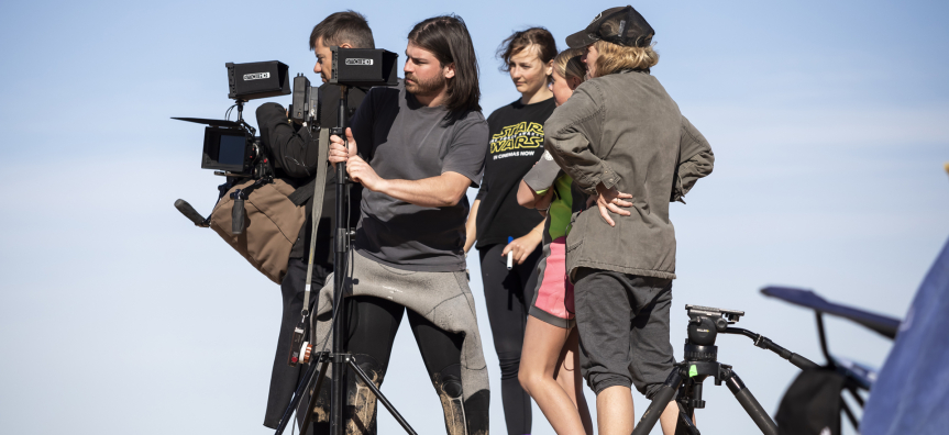 Photo of a film crew standing on a sandy beach.