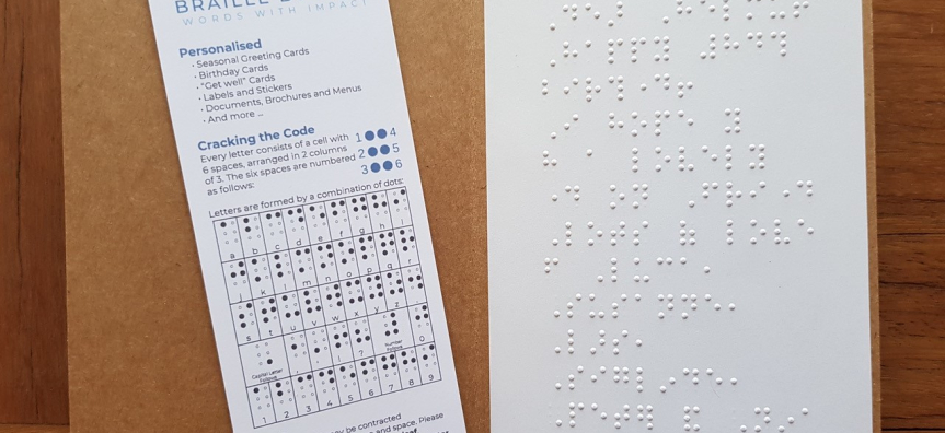A card with a braille message on the right, and a braille alphabet card on the left. 