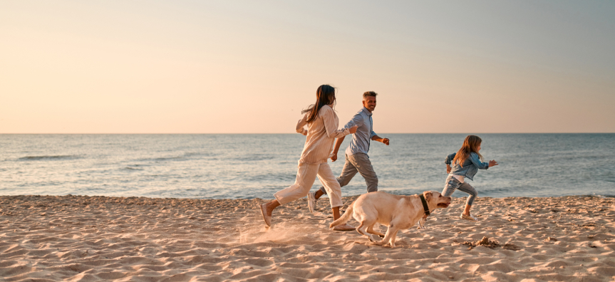 Two adults and a child running on the beach with a dog
