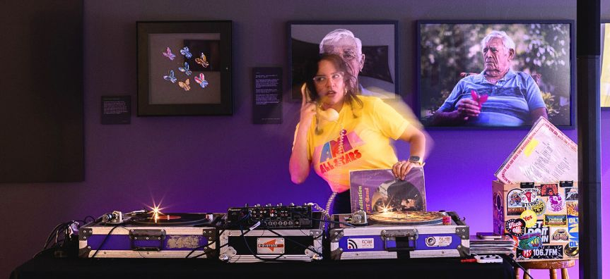 DJ standing behind turntable decks, slightly blurred while dancing, holding an spiral corded telephone.