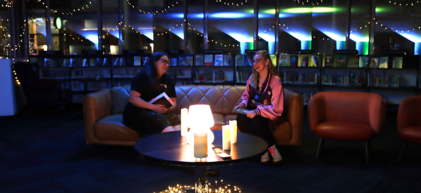 two people sitting on a couch talking in a library