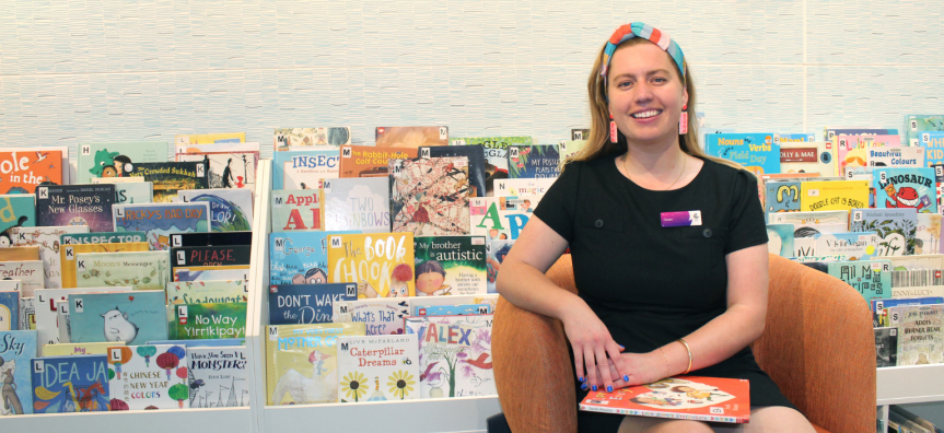 A Children's Presenter smiling, seated in front of the picture book collection.