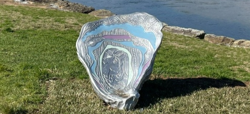 Metal shell artwork on grass next to beach