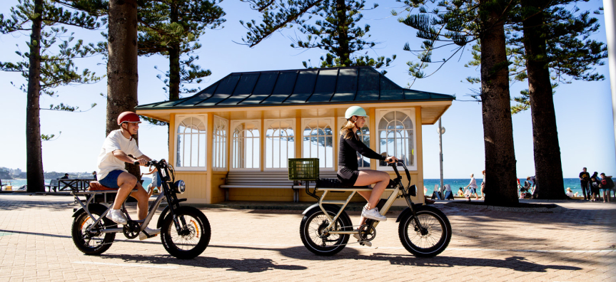 Two e-bikes users riding alongside the beach