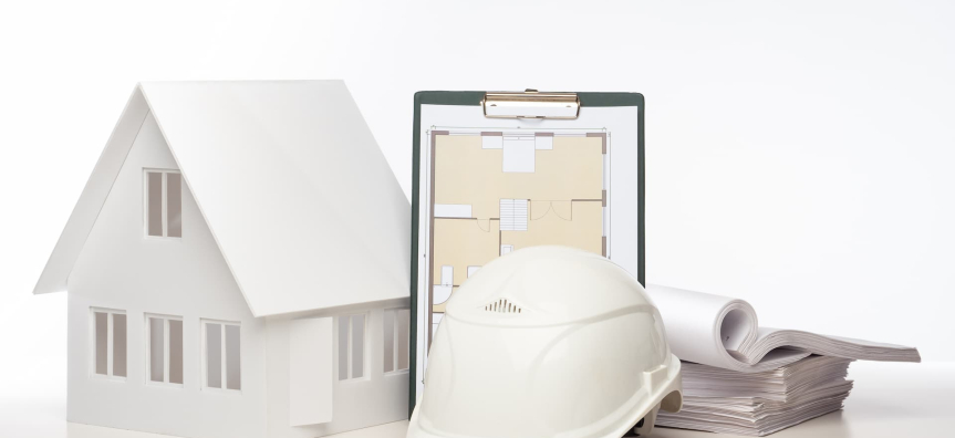 A boring stock image of bland white and beige drawings on a clipboard, a white cardboard model and a white protective helmet.