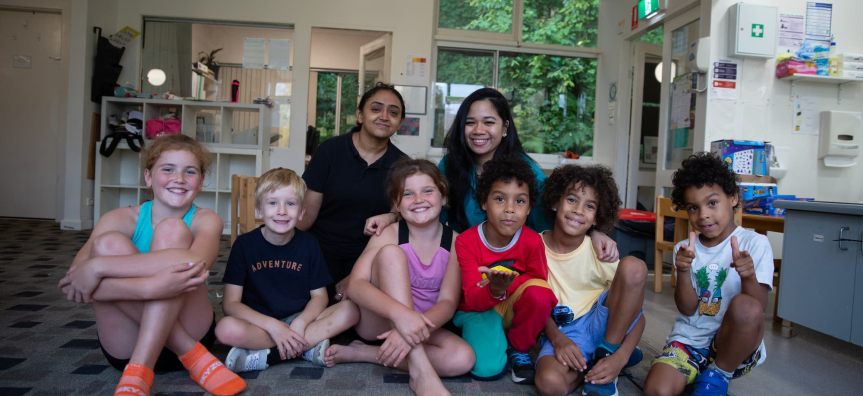  Children and adults of various ages sitting on the floor in a half circle at vacation care