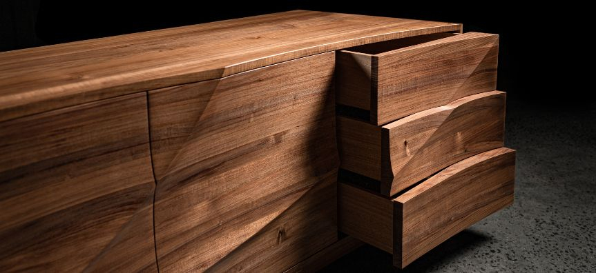 Close up of a solid dark timber low cabinet with draws, the façade sculpted with organic lines undulating across the surface