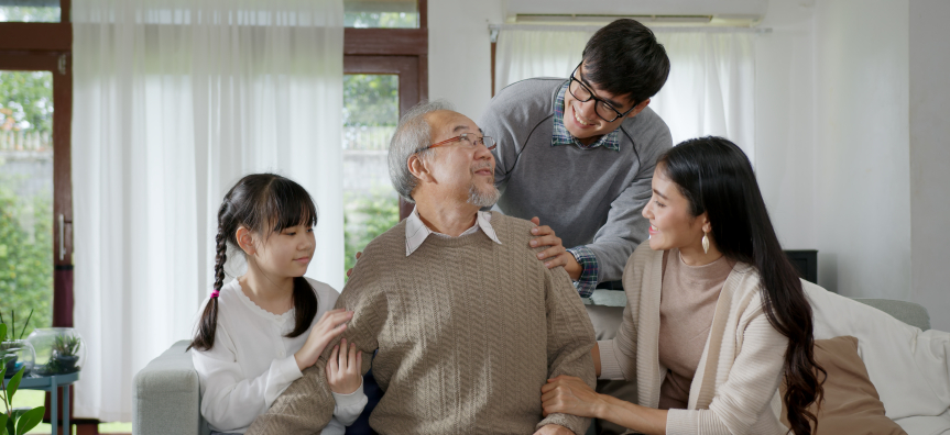 Older man smiling on the couch with his family smiling at him