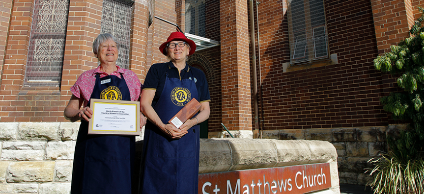 Country Women's Association Manly members Diana and Robyn stand in front of St Matthews Church holding their award