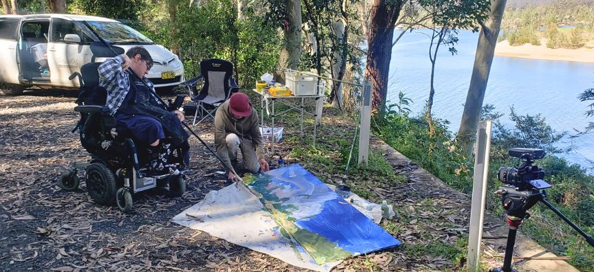 Matthew Elliott with Zachariah Fenn, painting on the side of the road, overlooking a curving river at Bundanon