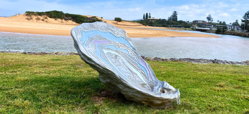 Metal shell artwork on grass next to beach