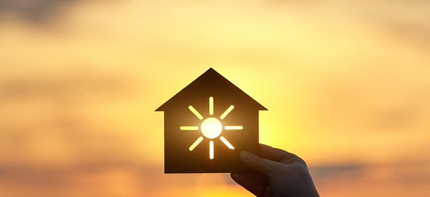 A hand holding a house cutout with sunset shining through a sun sillouette