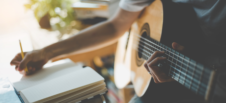 person with a guitar writing in a notebook