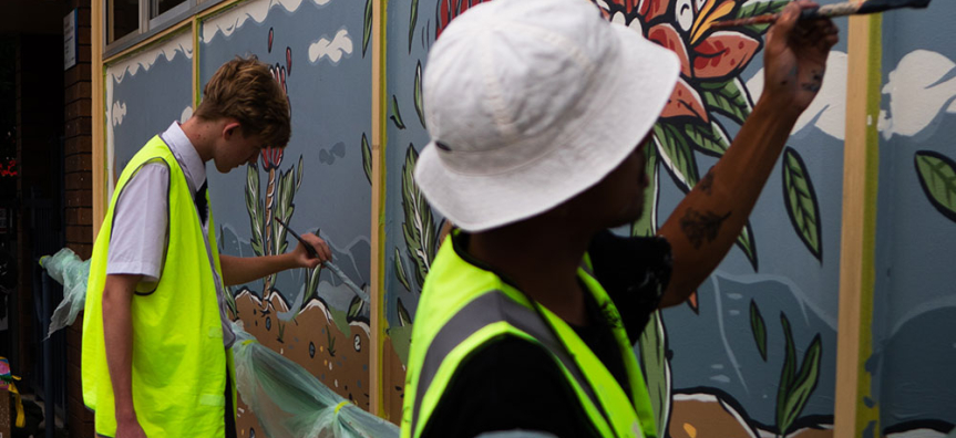 Two men painting a mural on an outdoor wall