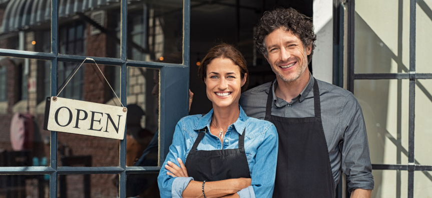 Two business owners standing outside their shop with the sign 'open'