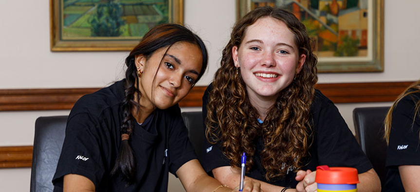 2 young people are smiling to camera while holding a pen