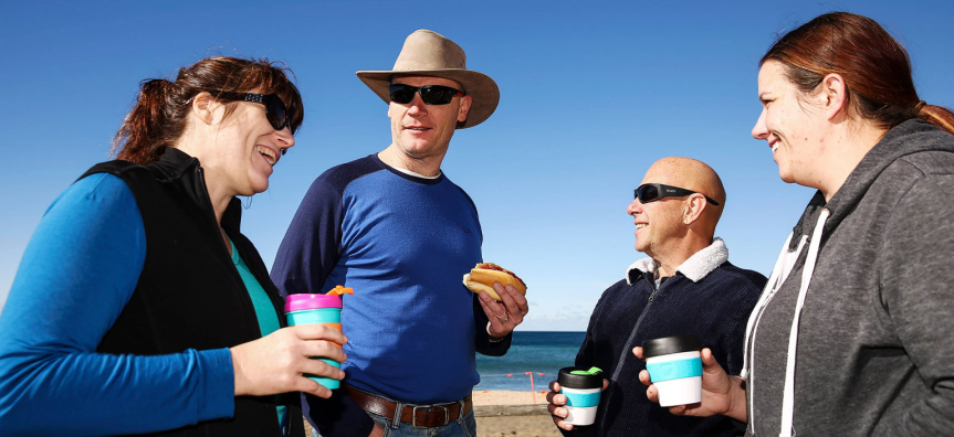 4 people drinking coffees out of keep cups and eating a hotdog bare