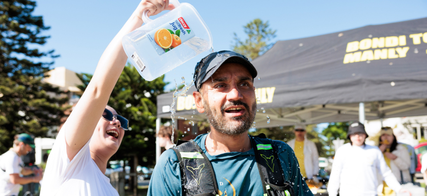 Bondi to Manly volunteer pouring water over a runner