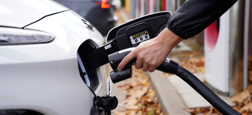A person's hand holding an EV charger and plugging it into a car