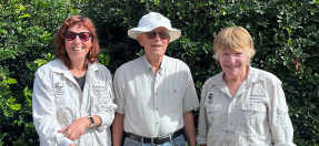 Three volunteers from the Curl Curl Community Garden dressed in their uniforms with bushland in the background