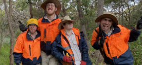 Four Bushlink workers are dressed in high visibility uniforms and smiling in a bushland setting