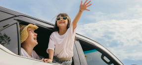 Young child and mother lean out of car window waving