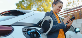 Young woman charges electric vehicle and looks at phone