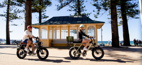 Two e-bikes users riding alongside the beach 