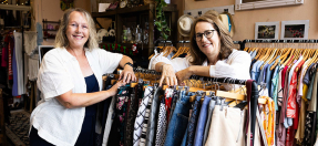 Owners of store Op for Change smile standing over racks with clothes for sale