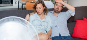 Couple sitting on a couch keeping cool with a fan 