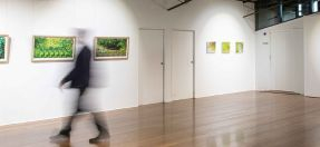 A blurred figure walks across an art gallery in front of abstract landscape photos