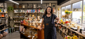 The owner of Queen B stands in her store with homemade products behind her